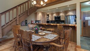 A wooden dining table with chairs, a chandelier, and a kitchen with wooden cabinets and appliances. - Walk to Ski & Village, Views Condo, Pool & Spa 315 (Mammoth Lakes)