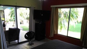 A hotel room with a bed, a TV, a chair, and a sliding glass door leading to a patio with a chair and a table.