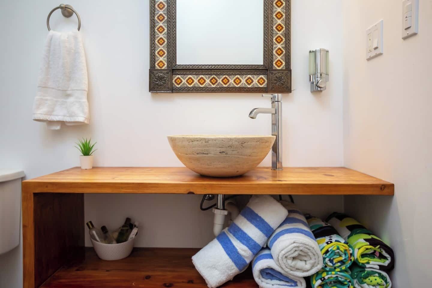 Un baño con tocador de madera, lavabo, toallero y una pequeña planta en maceta.