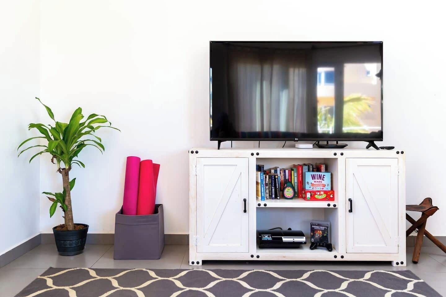 A living room with a television on a cabinet, a potted plant, and a stack of red mats.