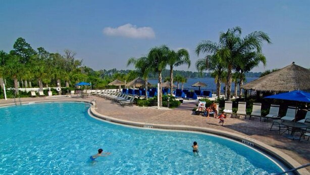 A swimming pool with lounge chairs and umbrellas, surrounded by palm trees and a view of the sea. - Quiet 2 Bedroom Resort Home (Davenport)