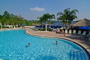Ein Pool mit Liegestühlen und Sonnenschirmen, umgeben von Palmen und Blick auf das Meer.
