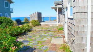 A stone pathway leading to a wooden house with a view of the ocean.