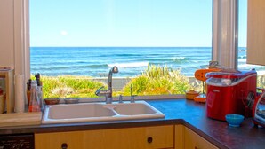 A kitchen with a large window overlooking the ocean, a sink, and a red appliance on the counter.