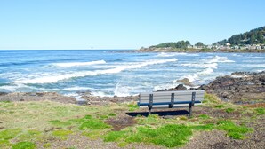 A bench by the ocean with waves crashing onto rocks.