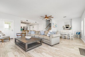 A spacious living room with a large sofa, a coffee table, and a dining area with a white table and chairs.