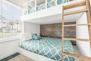 Un lit superposé avec une échelle en bois, des murs blancs et une fenêtre avec des stores.