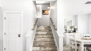 Una escalera de madera con barandillas blancas que lleva a un comedor con mesa y sillas.