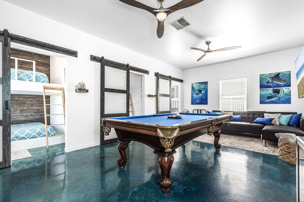 Une table de billard dans une pièce dotée d’un ventilateur de plafond, d’un canapé et d’œuvres d’art murales.