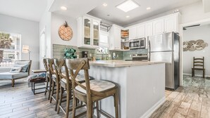 Una cocina moderna con armarios blancos, una isla central y una zona de comedor con sillas de madera.