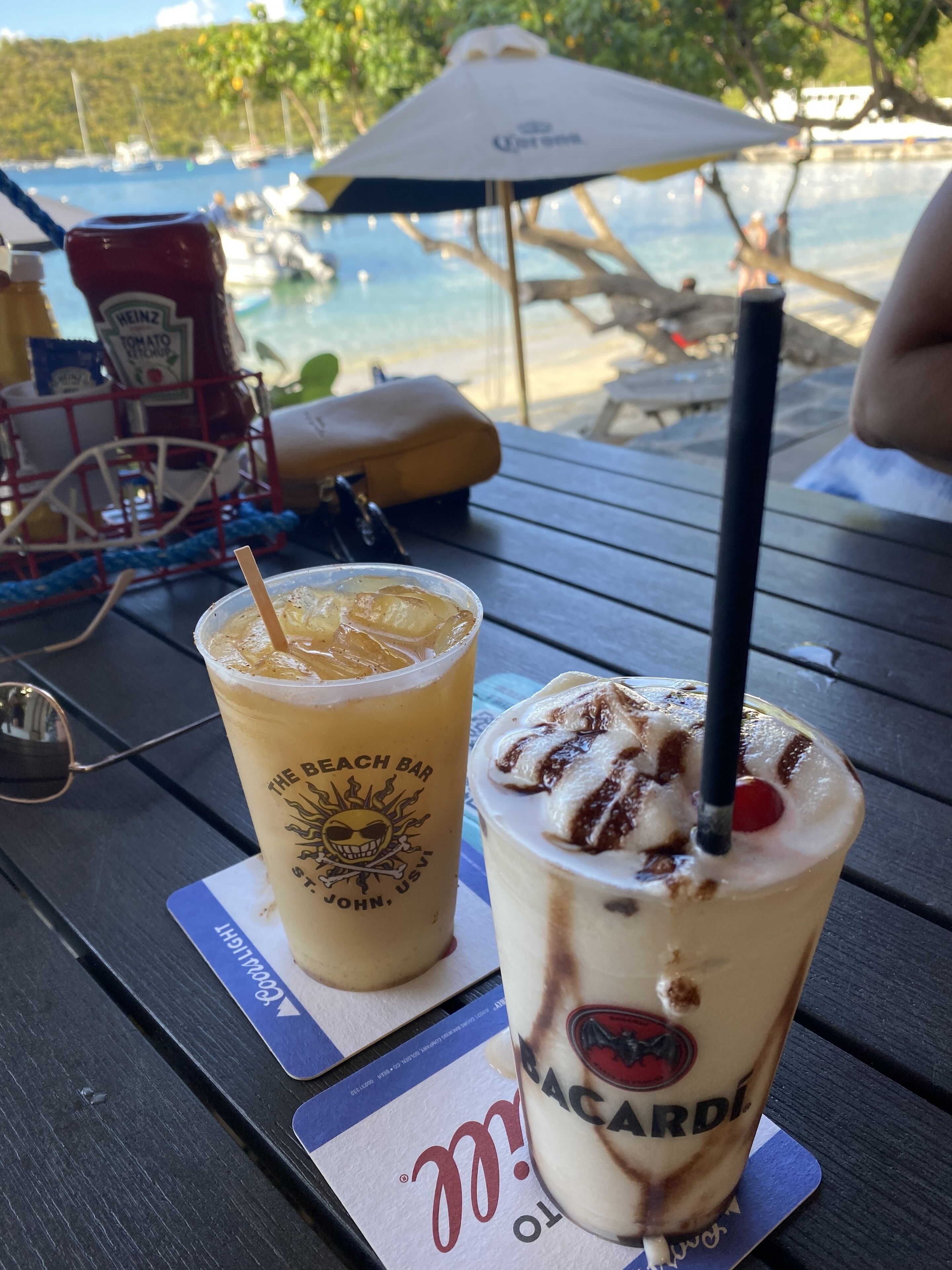 Ett bord med två drinkar, en flaska ketchup och ett strandparasoll.