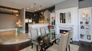 Una sala de estar moderna con una mesa de comedor de vidrio, sillas color beige, una chimenea y una cocina al fondo.