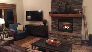 A living room with a stone fireplace, a flat-screen TV, a leather couch, and a coffee table with a candle.