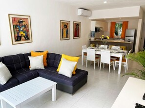 Ein Wohnzimmer mit einer Couch, einem Esstisch für vier Personen und einer Küchenzeile mit Kühlschrank und Mikrowelle.