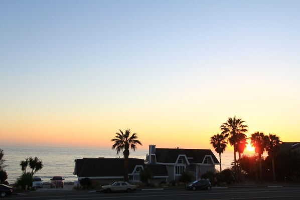 A coastal sunset view with palm trees and a building. - Impeccable Cape Cod Oceanfront Home Overlooking Swami's Beach. (Encinitas)