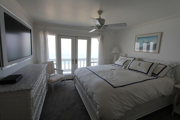A bedroom with a bed, a desk, a chair, a ceiling fan, and a window with a view. - Impeccable Cape Cod Oceanfront Home Overlooking Swami's Beach. (Encinitas)