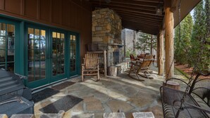 A covered patio with stone flooring, wooden furniture, and a stone fireplace. - Hot tub, Fireplaces, Game room, Rustic elegance, Private, 10 miles to AVL. (Fairview)