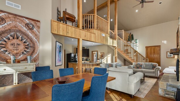 A spacious living area with a wooden staircase, a dining table with blue chairs, and a white sofa. - Hot tub, Fireplaces, Game room, Rustic elegance, Private, 10 miles to AVL. (Fairview)