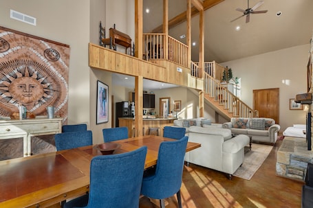 A spacious living area with a wooden staircase, a dining table with blue chairs, and a white sofa.
