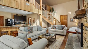 A spacious living area with a high ceiling, a wooden staircase, a kitchen with modern appliances, and a cozy seating arrangement. - Hot tub, Fireplaces, Game room, Rustic elegance, Private, 10 miles to AVL. (Fairview)