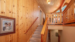 Een houten interieur met een trap, een ingelijst foto aan de muur en uitzicht door een raam.