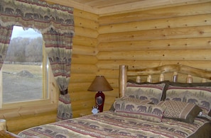 A log cabin bedroom with a bed, curtains, a lamp, and a window. - PO Ranch Log Cabin, close to Ski Area, rates subject to change for over 2 people (Salida)