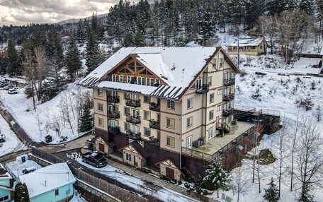 A multi-story hotel with a snow-covered roof, balconies, and a ski slope in the background.