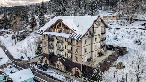 Un hôtel à plusieurs étages, dont le toit est recouvert de neige, avec des balcons et une piste de ski en arrière-plan.
