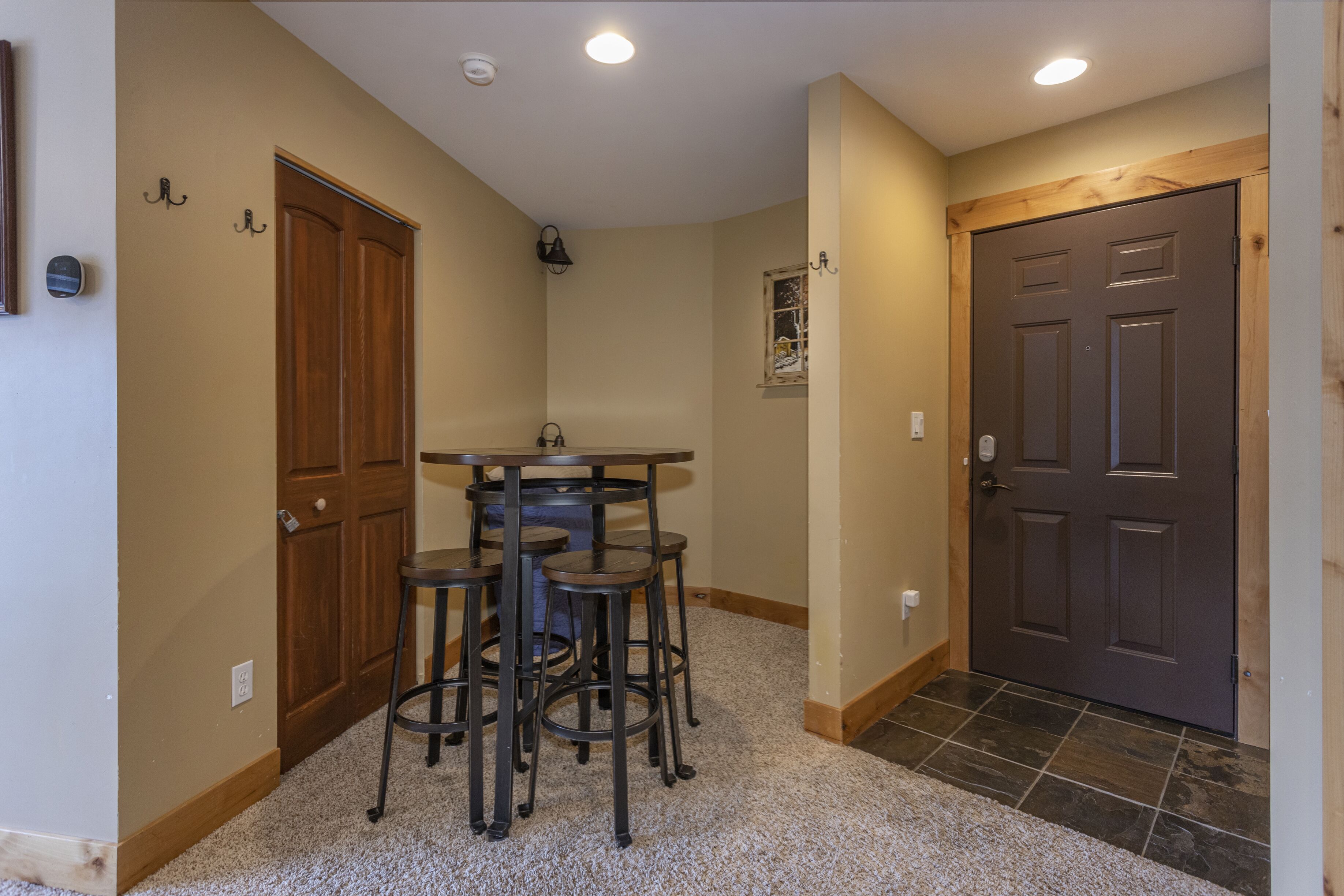A hallway with a wooden door, a small window, and a table with stools.
