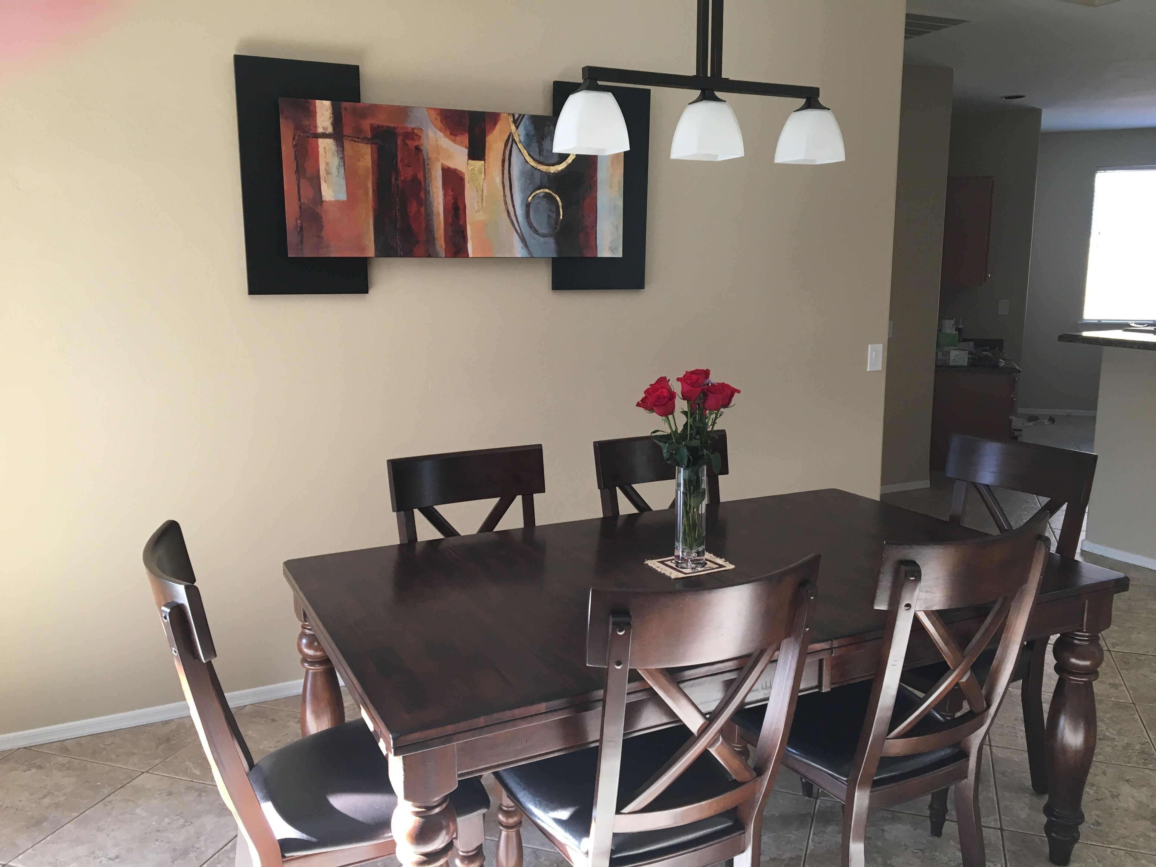 Un coin repas avec une table en bois foncé, six chaises, un vase de roses rouges et un tableau abstrait moderne accroché au mur.