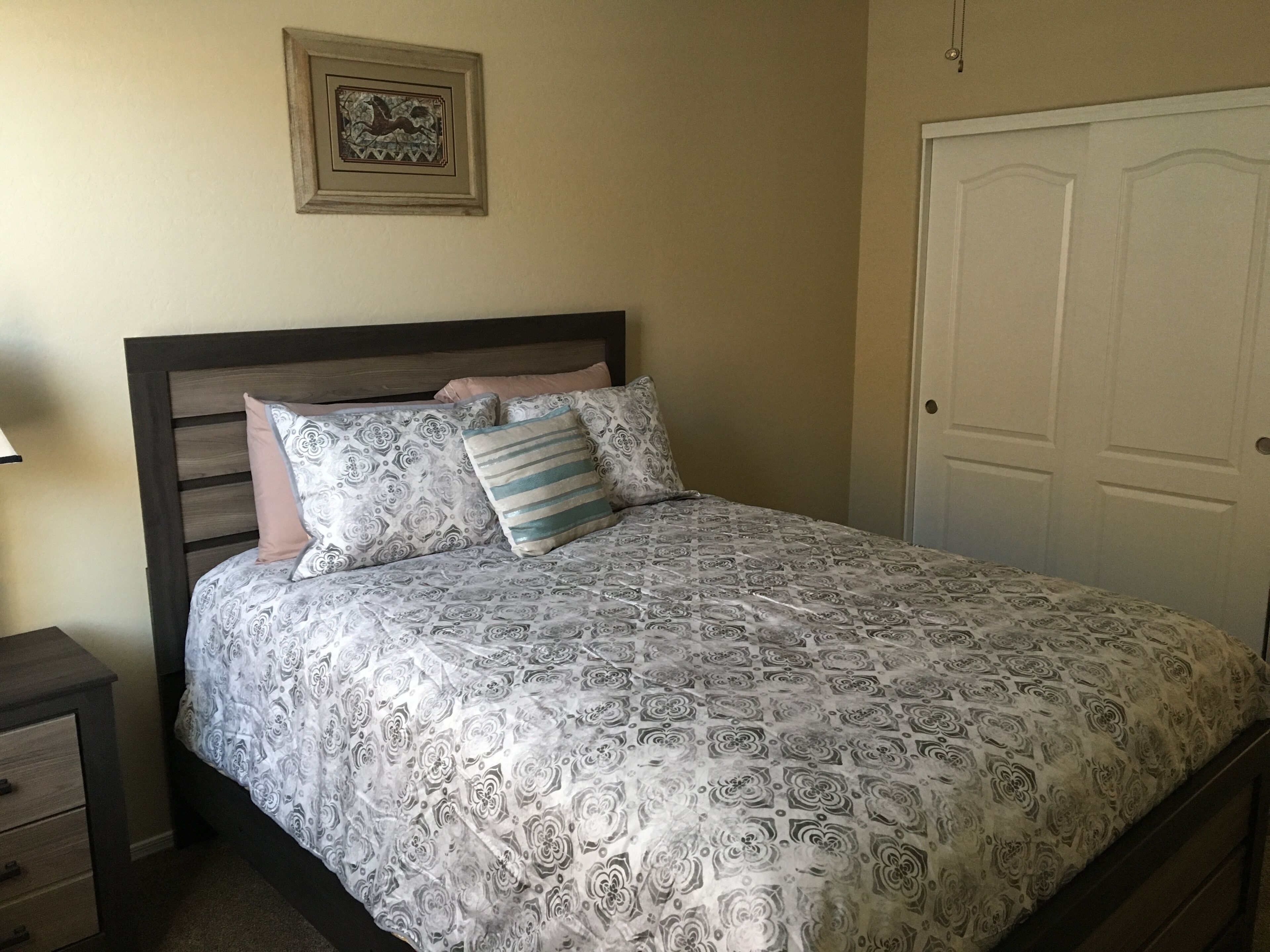 A bedroom with a bed, a nightstand, a dresser, a door, and a framed picture on the wall.