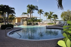Relax by the calm pool surrounded by palm trees and lounge chairs.