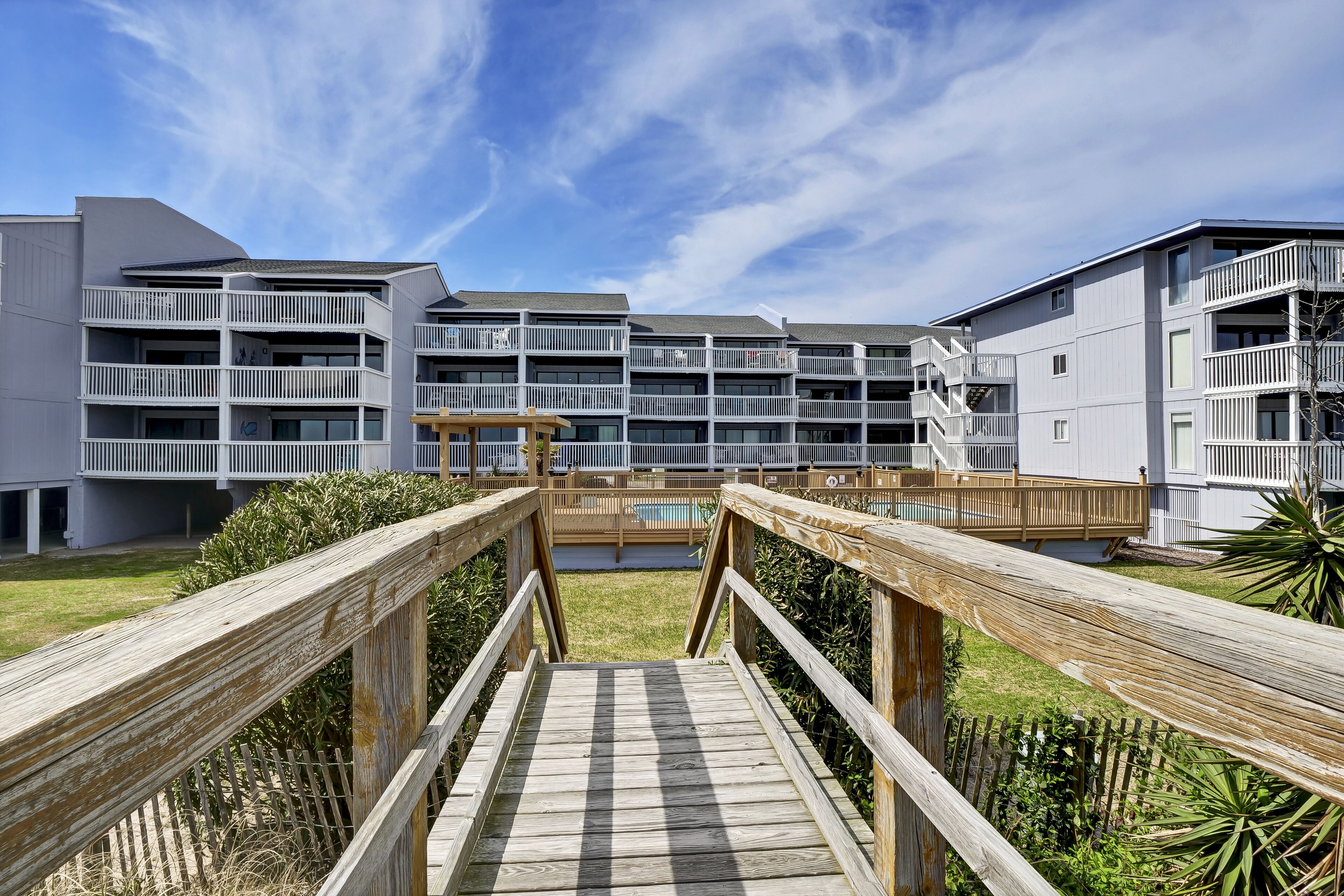 Ein modernes, mehrstöckiges Gebäude mit Balkonen und einer Holzterrasse, die zu einem Poolbereich führt.