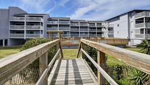 Een modern meerhoog gebouw met balkons en een houten terras dat leidt naar een zwembad.
