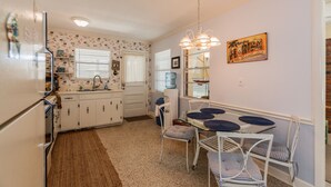 A compact kitchen with white cabinets, a refrigerator, a dining table with blue chairs, and a water dispenser.