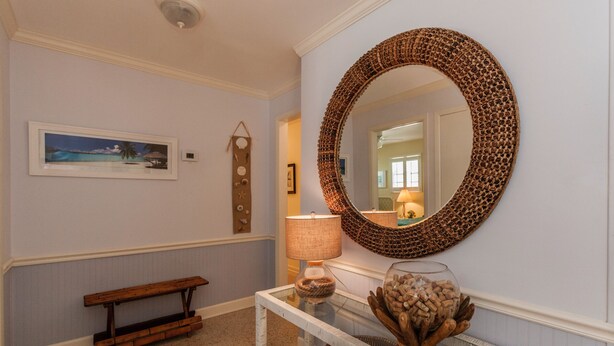 A hallway with a round mirror, a bench, a table with a lamp, and a framed picture on the wall.