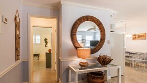 A hallway with a round mirror, a wicker basket, and a table with a lamp.