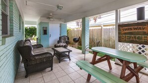 A covered patio with wicker furniture, a wooden picnic table, and a sign indicating the direction to the beach.