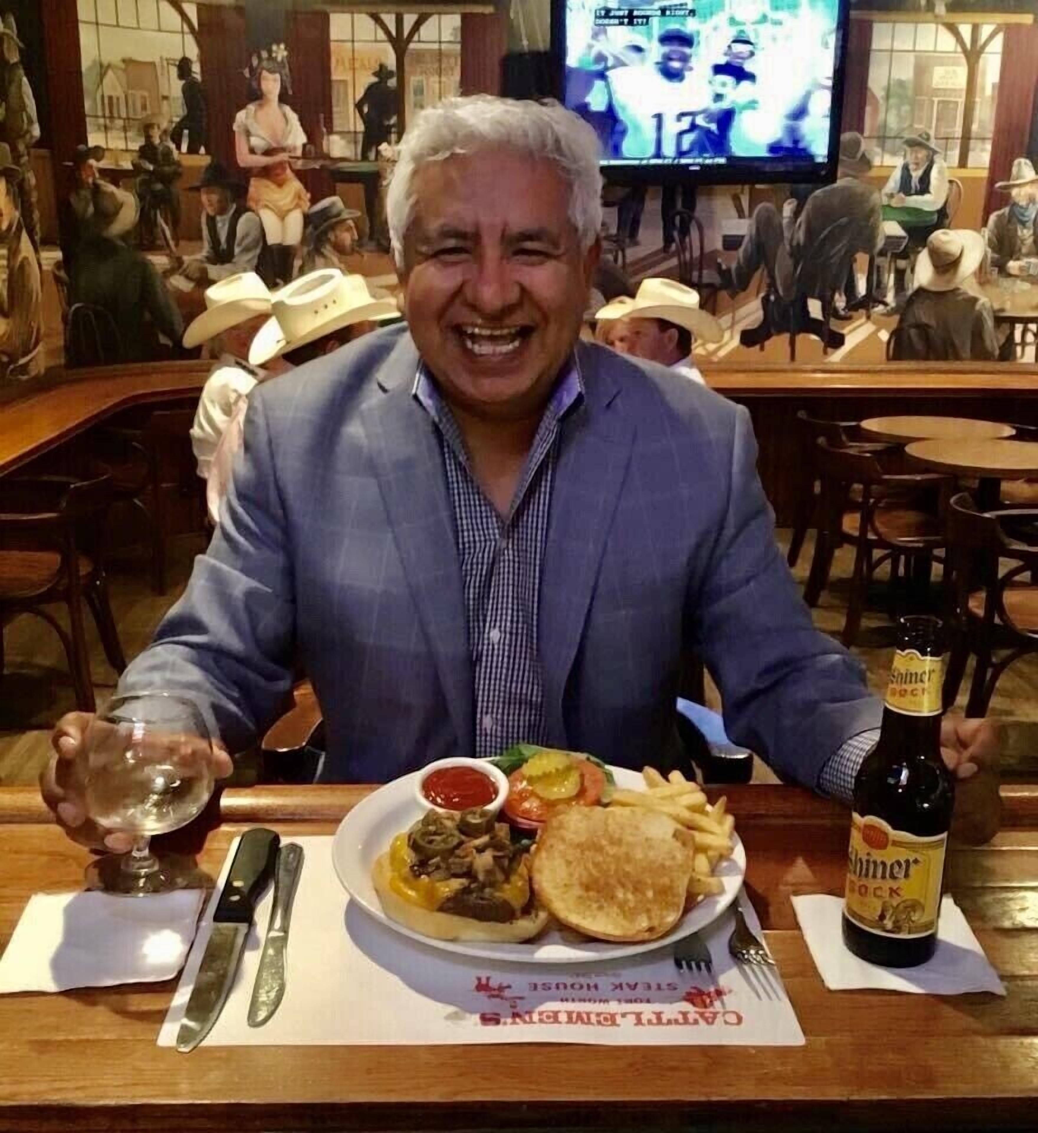 Un homme est assis à une table devant un repas, une bouteille de bière et un verre de vin.