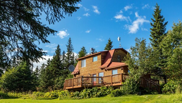 A two-story cabin with a balcony, surrounded by lush greenery and tall trees. - Moose Meadows near Kilcher Homestead in Alaska the Last Frontier (Homer)