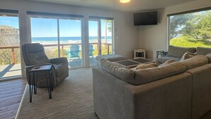 A spacious living room with a large gray sectional sofa, a recliner, and a small table. There are large windows offering a view of the ocean. - Starr Creek - Ocean and Creek right outside! (Yachats)
