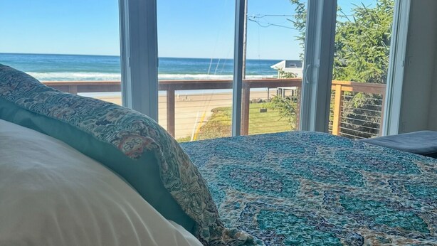 A bedroom with a large bed, a view of the ocean, and a balcony. - Starr Creek - Ocean and Creek right outside! (Yachats)