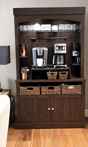 A dark wooden cabinet with a coffee maker, mugs, and baskets.