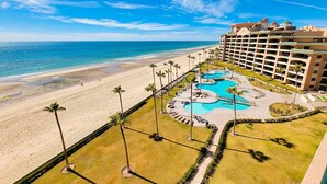 A resort with a beach, a pool area, and a large building with multiple balconies.