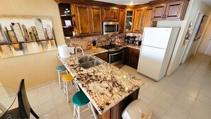 A kitchen with wooden cabinets, a marble countertop, a sink, a stove, and a refrigerator.