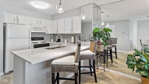Une cuisine moderne avec des meubles blancs, un îlot central et un coin repas doté de chaises en osier.