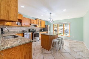 A kitchen with wooden cabinets, granite countertops, stainless steel appliances, and a large window with a view of trees.