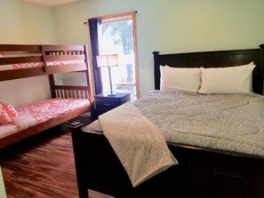 Una stanza con un letto a castello, un letto singolo con copriletto decorato, un comodino con lampada e una finestra con tende.