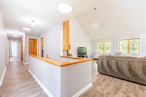 A spacious living area with a wooden accent wall, a built-in TV, and a large window providing natural light.