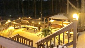 Lumipeitteinen terassi, jossa on katettu huvimaja, puiset kaiteet ja ulkovalaisimet.
